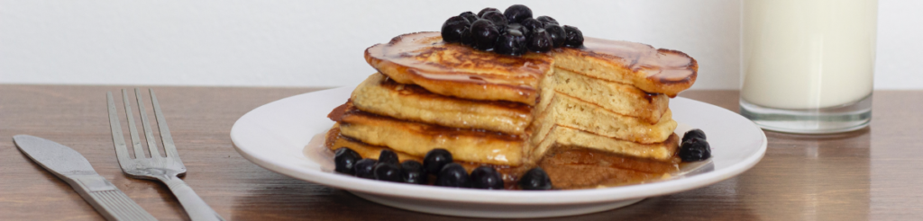 A plate with a stack of blueberry pancakes and a glass of milk